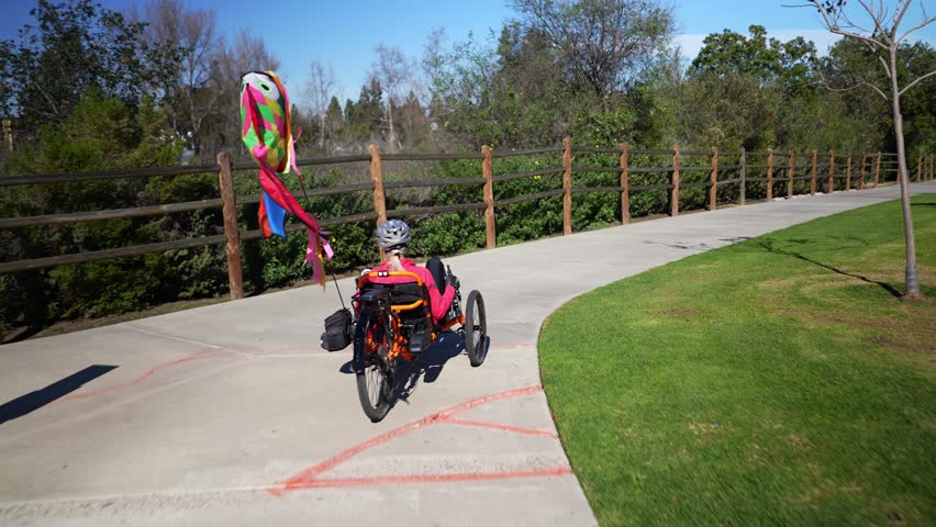 Elderly senior woman riding recumbent tricycle e-bike on a path on a sunny day in a park.