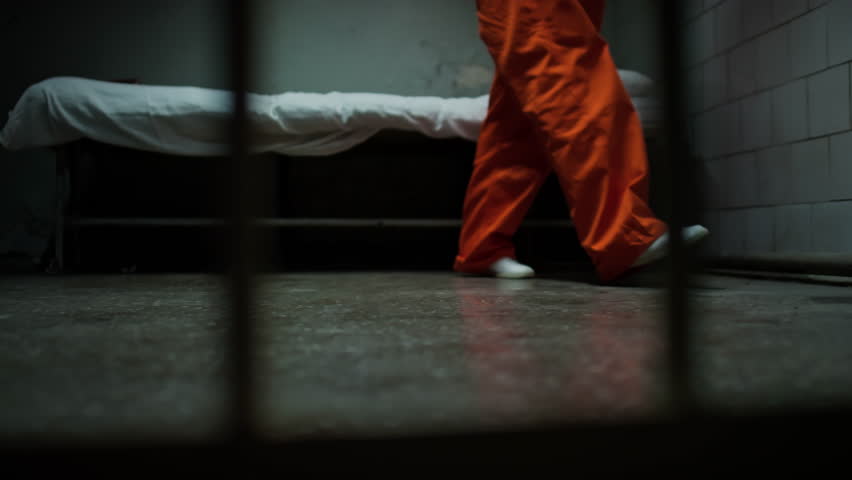 Low section shot through bars of legs of anxious inmate in orange jail uniform pacing around prison cell Royalty-Free Stock Footage #3429022279