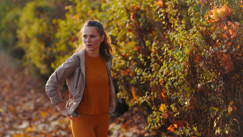 Hello autumn. Full length portrait of tired stylish woman in fitness clothes in the park relaxing after workout.