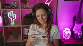 A smiling caucasian woman wearing headphones texts indoors at a gaming setup during the night.