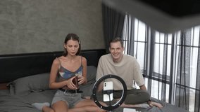 Young woman making beauty and cosmetic tutorial video content for social media using her boyfriend as model and light ring. Beauty blogger showing how to beauty care to audience or follower. Adit
