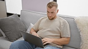 A young bearded man works on his laptop in a modern apartment living room, then gestures no to the camera.