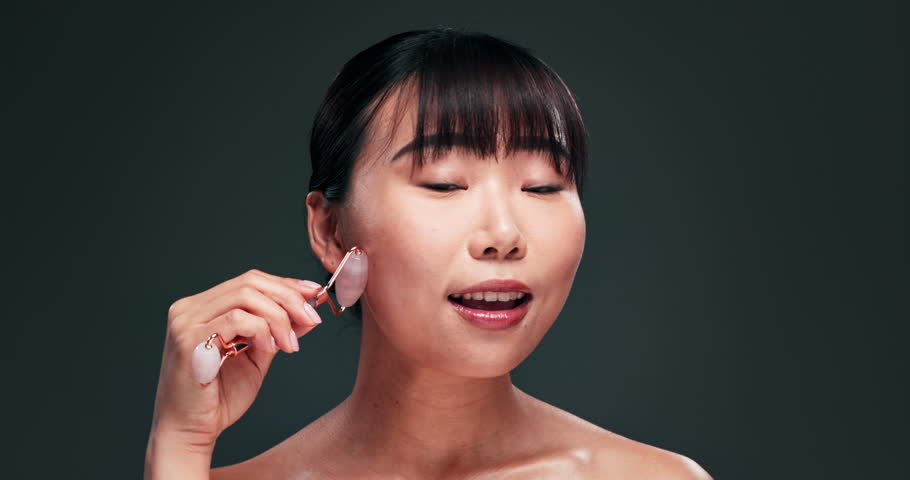Beauty, smile and jade roller for face with asian woman in studio on dark background for skincare or wellness. Portrait, massage or antiaging and happy young person with product for dermatology Royalty-Free Stock Footage #3429140537