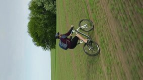 Vertical video. An adult Caucasian man rides an MTB bike across a field.