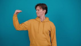 Young man shows bla-bla-bla gesture. Guy in yellow jacket imitates talking with hand, standing on blue background in studio. Babbling