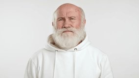 A video of an elderly man in a white hoodie touching his forehead and squinting in pain, showing clear signs of a headache against a plain white background. Camera 8K RAW. 