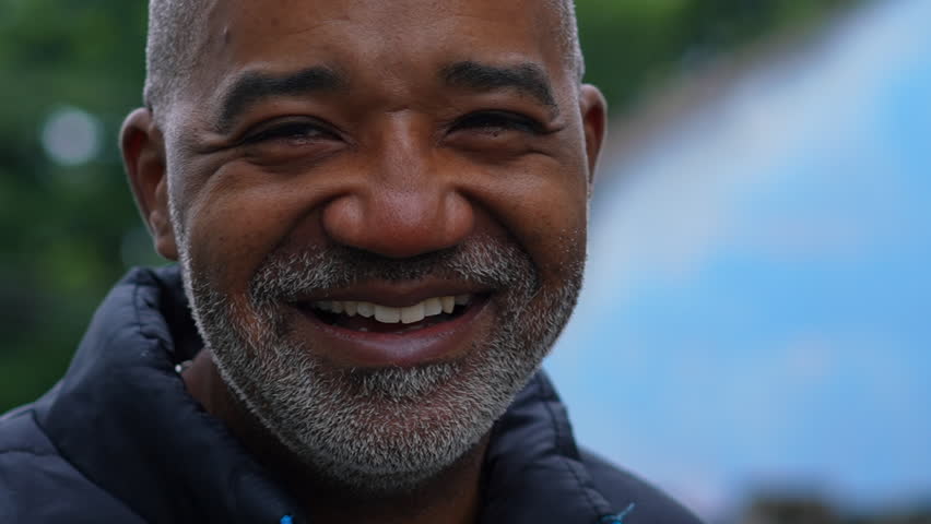 One joyful black middle aged man close-up face smiling at camera in tight tracking shot in urban environment. Gray hair African American person in 50s in street Royalty-Free Stock Footage #3429347405