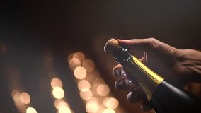 Champagne explosion. Champagne popping, opening champagne bottle closeup. Sparkling Wine over Holiday Bokeh Blinking Background. Party, Success, holiday celebrating. Slow motion UHD 4K