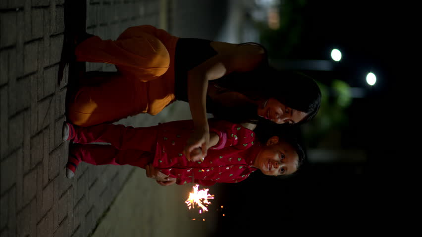 Vertical slow motion of a lovely latin child with his mother playing with bengal lights celebrating christmas eve in Mexico