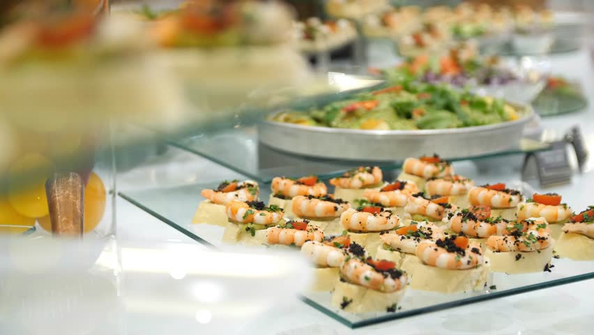 Close-up of beautifully presented buffet table with canapes, vegetables and herbs in a restaurant. Canapes with shrimps and vegetables on a banquet table. Catering service. Buffet table food. Royalty-Free Stock Footage #3429567939