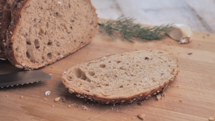 A man puts smoked salmon on a piece of bread and adds a sprig of dill on a wooden cutting board