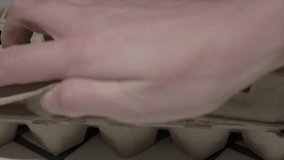 This close up video shows an egg carton being opened and a hand taking eggs out.