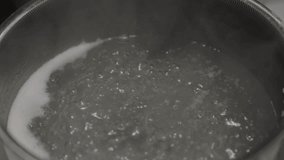 This video shows an egg being placed in a boiling pot of water with a kitchen spoon. 