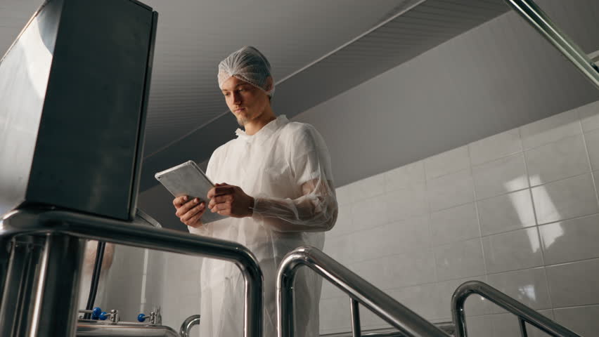 A male technologist in a protective suit with a tablet in his hands checks the production stage of fermentation of a drink at a brewery Royalty-Free Stock Footage #3429634835