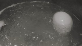 This close up video shows an egg being placed in boiling water and cracking upon submersion.