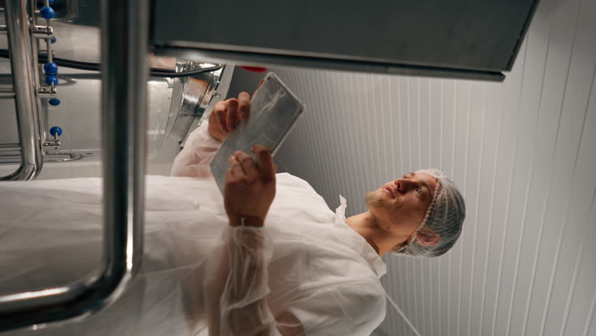 vertical video A male technologist in protective suit with a tablet in his hands checks the production stage of fermentation of a drink at a brewery Royalty-Free Stock Footage #3429642433