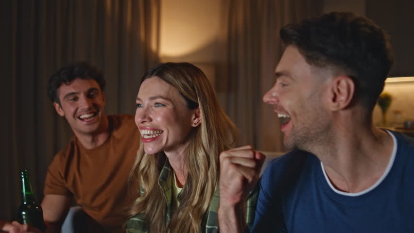 Laughing mates enjoying beer at weekend evening meeting close up. Excited friends clinking bottles at night friendly gathering together. Happy group young people partying with alcohol in living room.