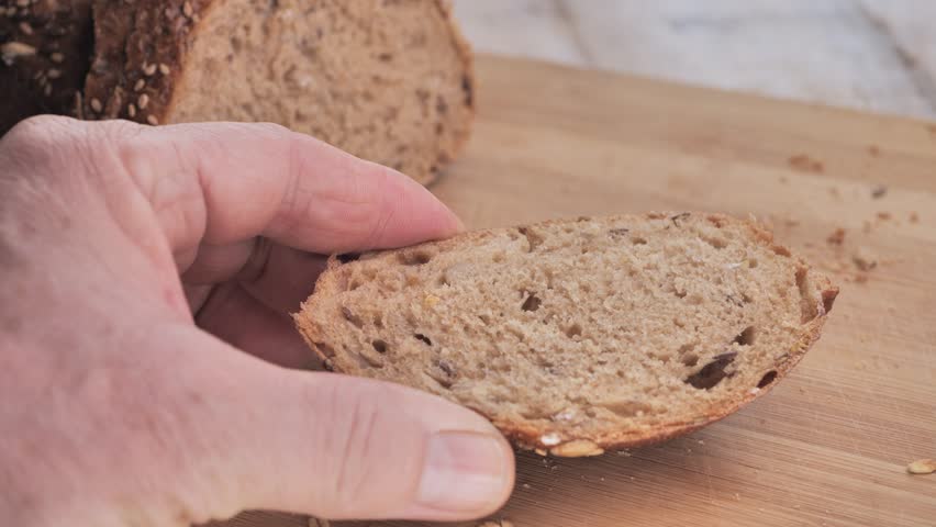 A man puts a vegetable salad on a piece of bread and adds a sprig of dill on a wooden cutting board