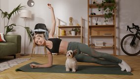 Happy caucasian woman improving balance with side plank pose with beaver yorkshire terrier indoors. Active female doing sports and spending time with furry family member in living room. - Powered by Shutterstock - Get 15% off with code: PIKWIZARD15