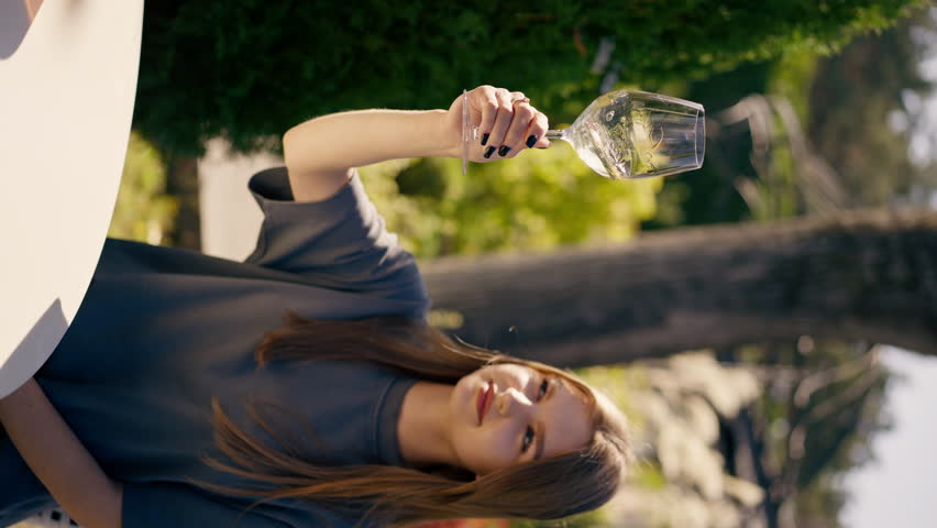vertical video A young beautiful girl holds a glass of wine in her hand and carefully examines it determine the quality of drink