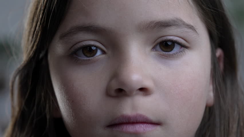 Macro tight close-up of child's face looking at camera with solemn blank expression. Little girl portrait