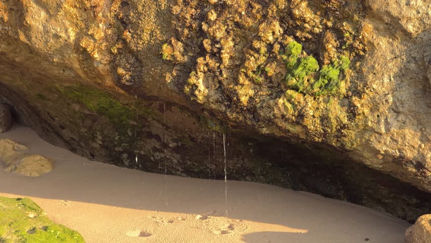 Water cascades from rocky structures, showering droplets upon the stony surface. A daytime snapshot highlighting the allure of nature in motion.