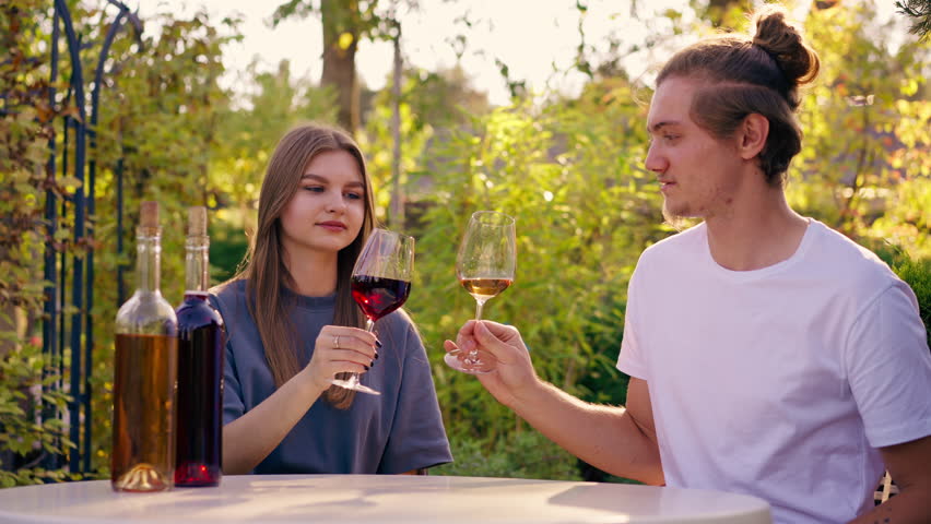 A couple of a guy and a girl are sitting together at a table in garden of a winery tasting different types of wine