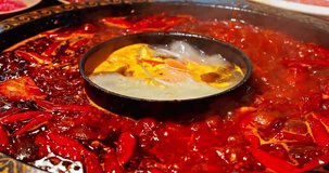 Chinese spicy hot pot cuisine. A layer of red chili pepper floats in the boiling hot pot base. 4K Real time video.