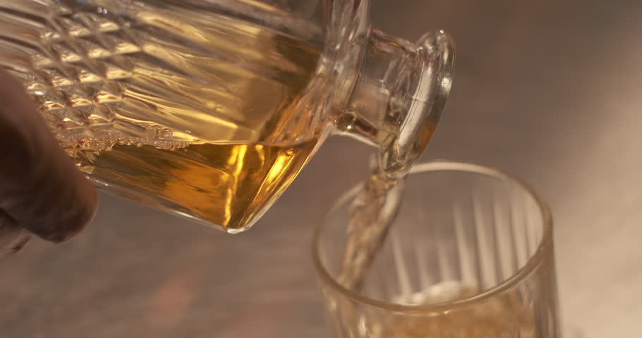 Close-up pouring whiskey into glass from the decanter