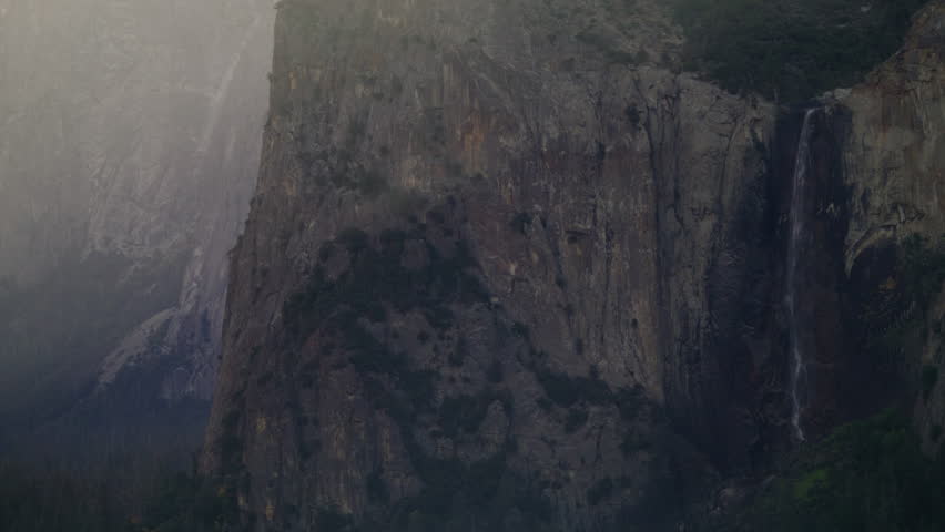 A misty waterfall in Yosemite Valley cascades down a rugged mountain terrain, enveloped by the serene beauty of nature, Camera 4K RAW. 