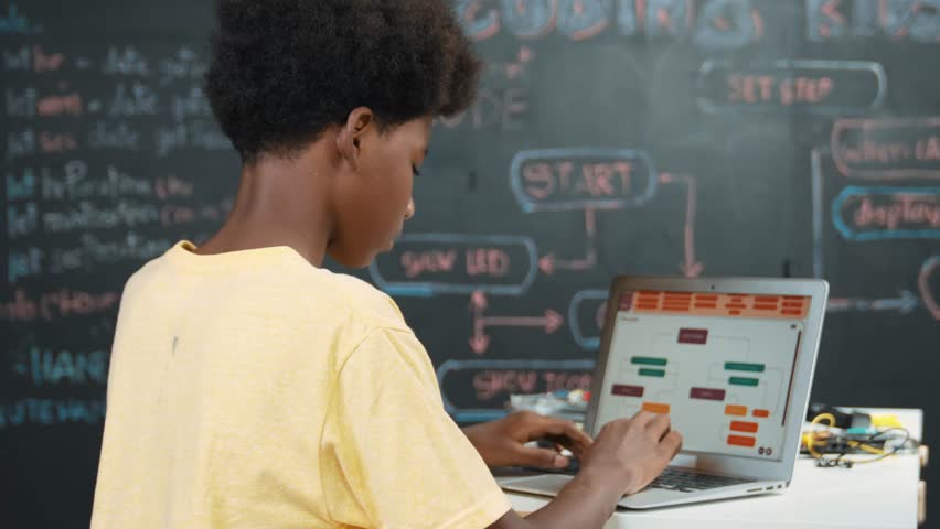 Back view of african boy programming system or coding system. Professional high school student working learning to write engineering code while sitting blackboard. Creative education. Edification