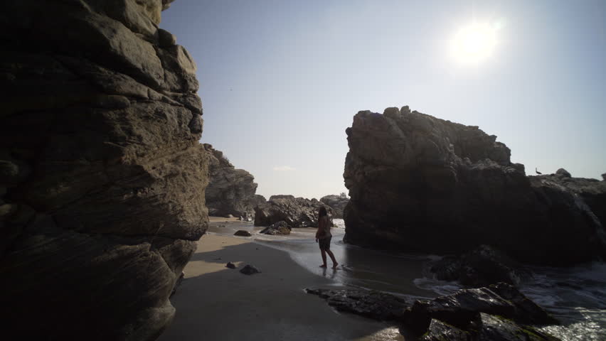 pov , follow the young women, in silhouette walking on beach with big cliff in sun shine