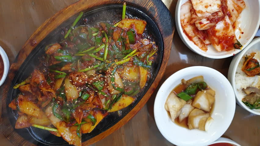 Local korean food hot plate sizzling pig organ head offal and skin spicy sauce with side dishes top view slow motion