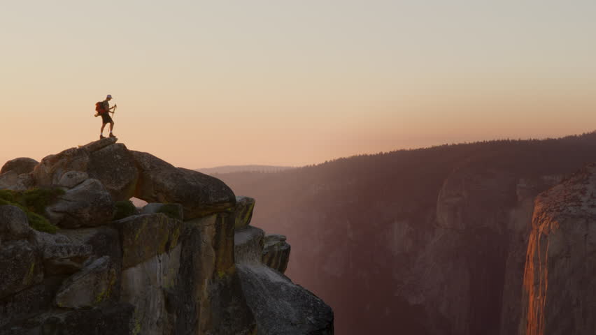 The silhouette of an ecstatic hiker stands on a rocky mountain edge, arms outstretched, embracing the vastness at dusk. Yosemite national park. Slow Motion, Camera 4K RAW.  Royalty-Free Stock Footage #3429944439