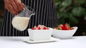 Pour the milk into the strawberry bowl. Delicious fresh milk with strawberries in a white plate and a glass of milk
