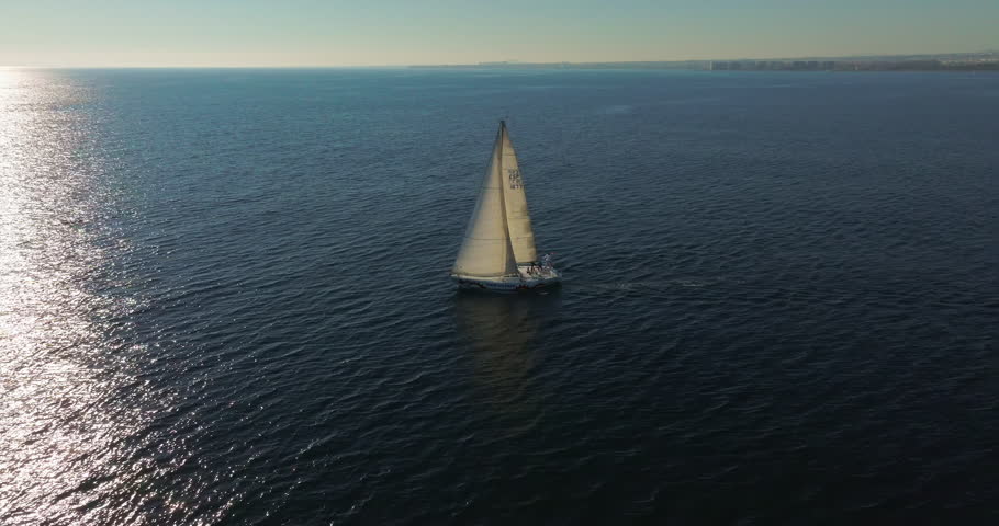 Tracking shot following a yacht into the sunset. Big sailing yacht boat driving on the ocean on a sunny day. Floating sailing yacht with spread sails splitting the sea waves