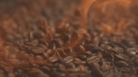 Super slow motion shot of falling hot roasted coffee beans with smoke in macro. Roasting and burning flying whole coffee with fire. Close up video