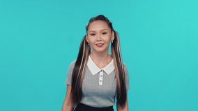 Young Asian woman dances to the music on a blue light background and takes video of herself on smartphone for a social network.