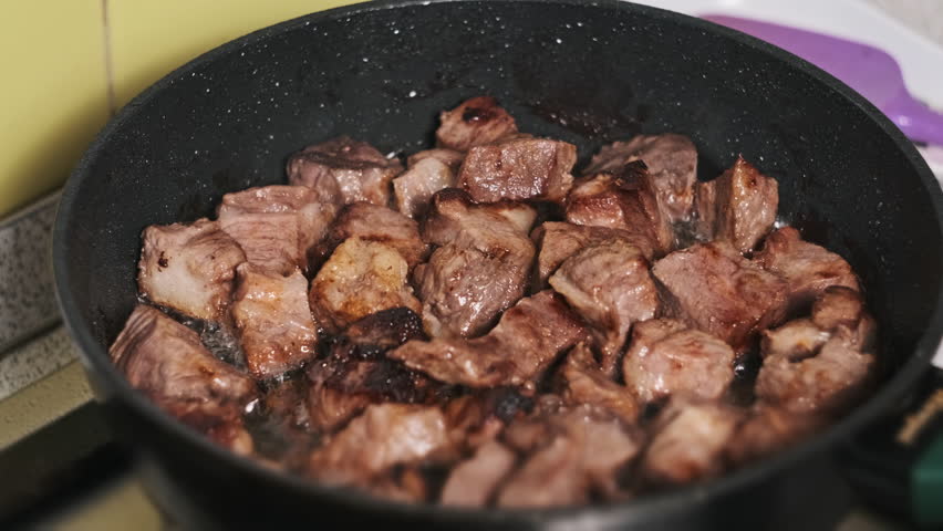 Pieces of pork meat are fried in a frying pan in a home kitchen. Appetizing juicy chopped meat is cooked and roasted on a non-stick frying pan on the stove. Food preparation