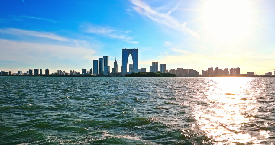 Suzhou skyline and modern city buildings scenery at sunset by the lake. Beautiful Jinji Lake landscape in Suzhou. 4K Real time video.