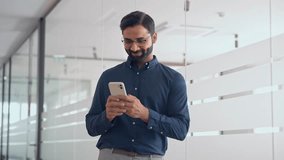 Smiling Indian businessman using mobile cell phone working standing in office. Happy professional business man making banking transaction payment on smartphone working on cellphone at work. - Powered by Shutterstock - Get 15% off with code: PIKWIZARD15