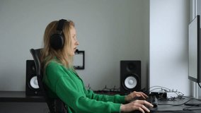 Side view of woman with headset playing online computer games. Female gamer. Esports. Domestic apartment.