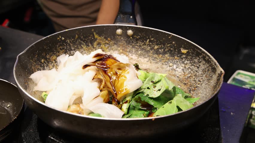 Fresh Thai food frying in pan. Cooking Pad See Ew at a night market in Thailand. Street food and Thai culture. Vegetables, egg and noodles stirred in skillet.