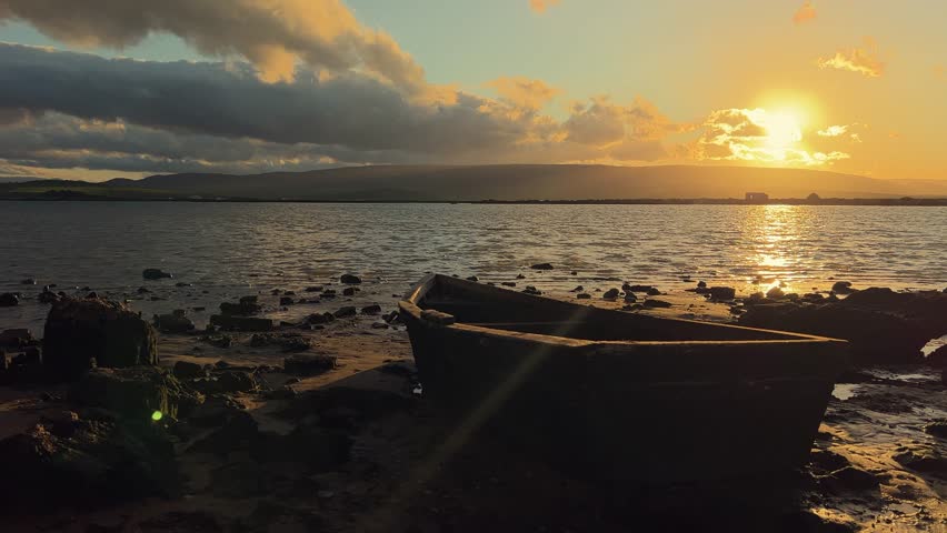 Time-lapse of a small boat on a tranquil bank with the sun setting behind scattered clouds