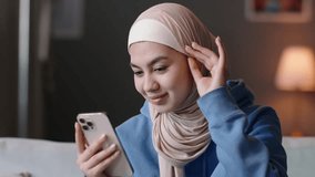 Woman adjusts hijab looking at smartphone camera. Muslim oriental woman gen z shows off on selfie camera, adjusts hijab before shooting recording video, taking selfie for social media networks. 