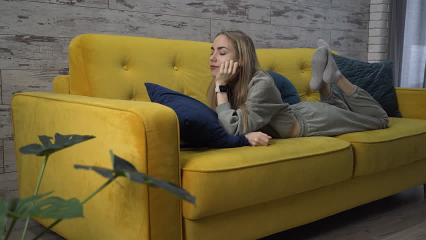 Woman is lying on a sofa in the living room and answering a call on a smartwatch. Starts talking