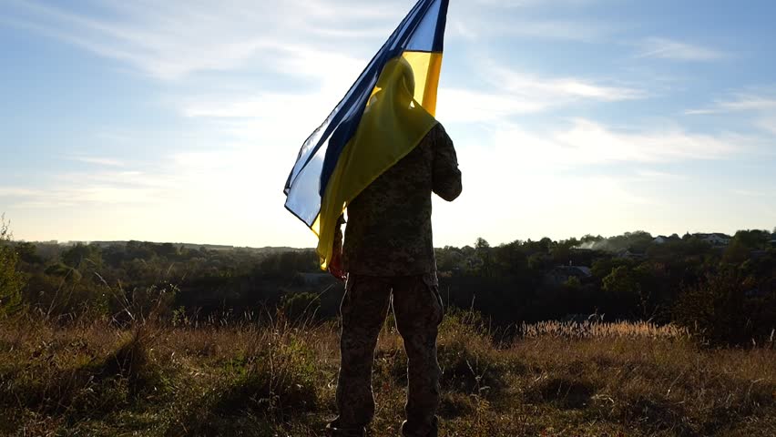 Ukrainian army man stands at hill with a national banner at countryside. Male soldier in military uniform with Ukraine flag as a symbol of victory against russian aggression. Invasion resistance Royalty-Free Stock Footage #3430272857