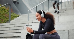 Fitness, phone and happy woman on headphones outdoor, typing in city or streaming radio by steps. Smartphone, sports and person listening to music on mobile app, video call or scroll on social media