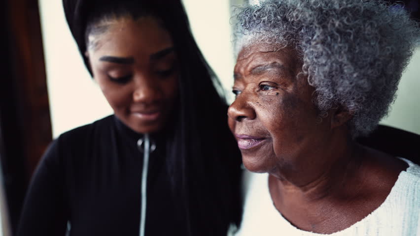 African American granddaughter hugging elderly 80s grandmother showing support and help for inter-generational family member. Family unity and love during old age