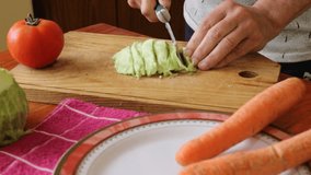 Typical vegan South American Argentinian foods, man prepares a vegan lunch on the wooden table at home, cuts cabbage with knife and tomato and carrots on a plate, beautiful healthy cooking video clips
